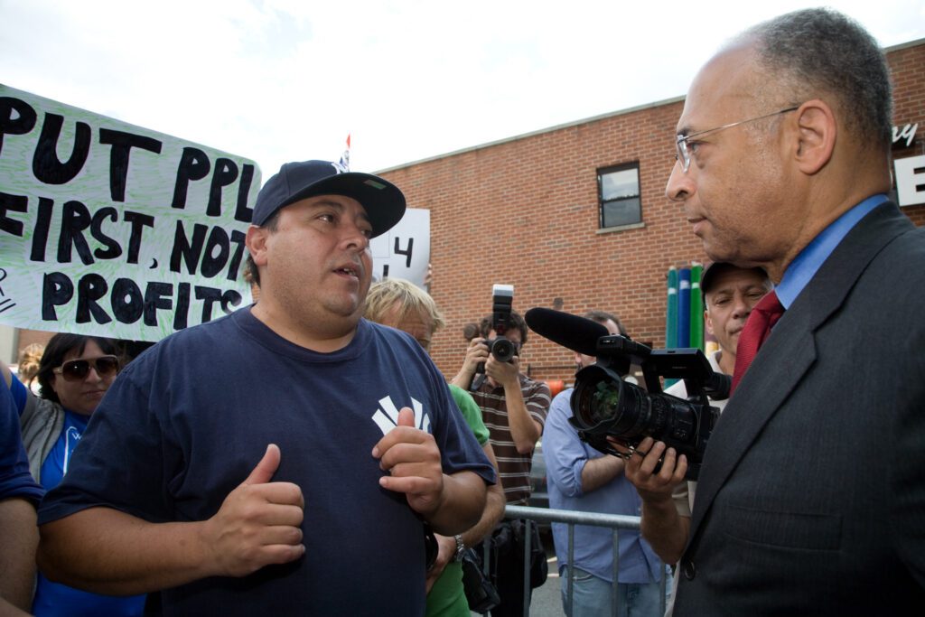 After a press conference outside the Stella D’oro factory, longtime employee Eddie Marrero (left) urges NYC Comptroller and mayoral candidate William Thompson Jr. (right) to follow through on his promise to help the workers. "Stella D'oro Workers Fight for Jobs," from The Clarion (Professional Staff Congress, City University of New York).